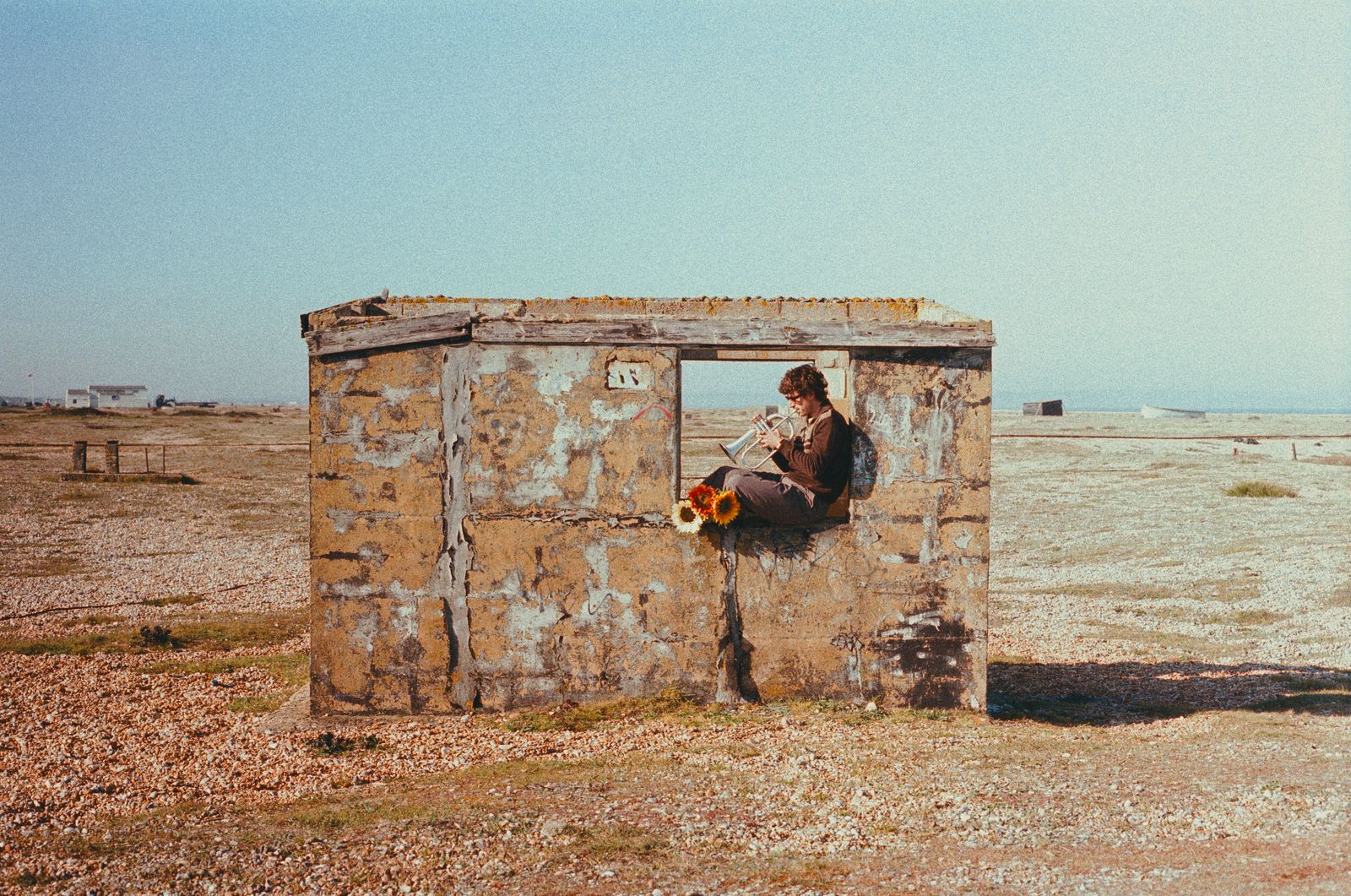 Sol Paradise playing trumpet inside a weathered beach shed, wide shot